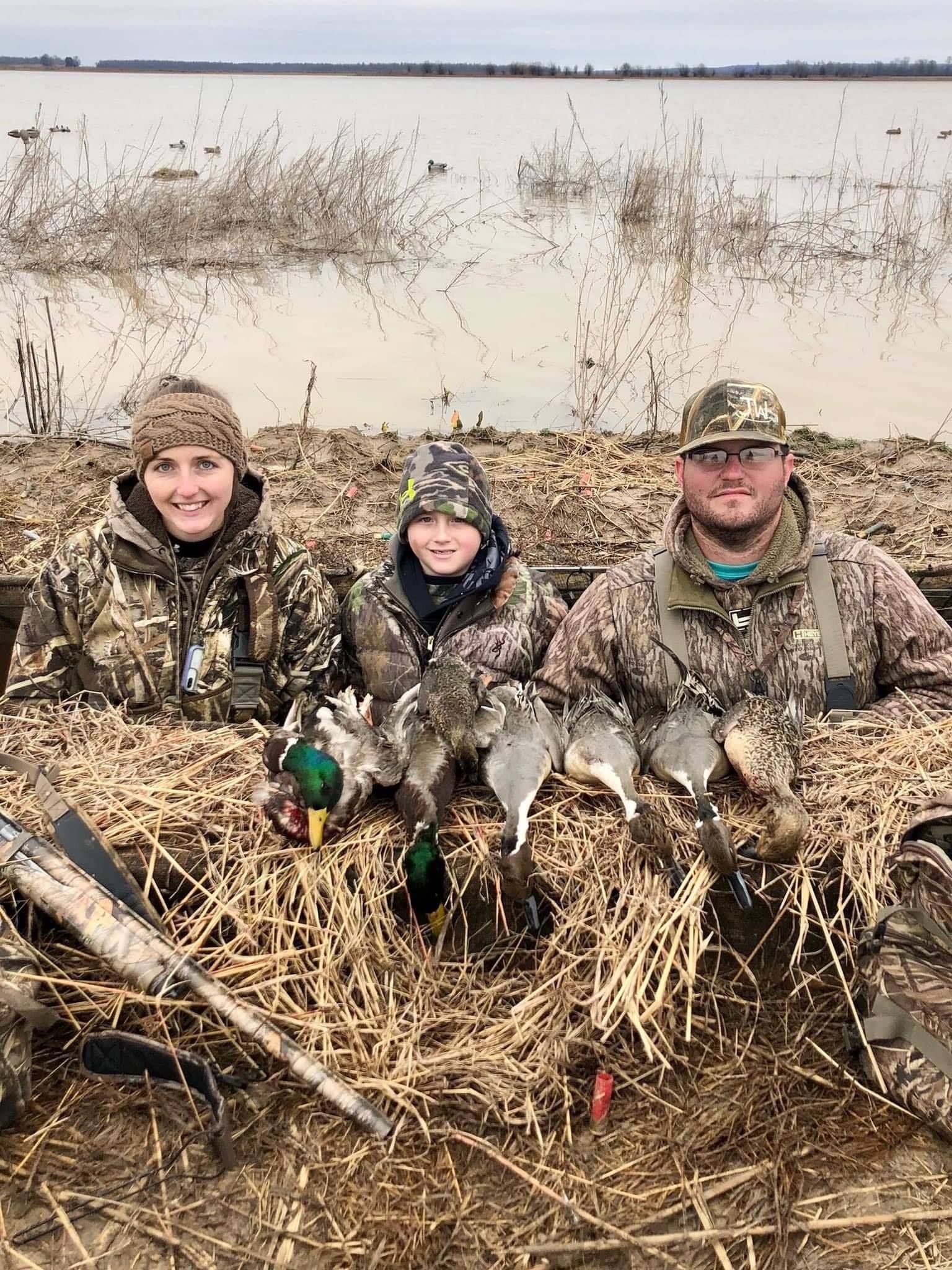 Three camouflaged hunters posing with ducks in a marsh after a waterfowl hunt