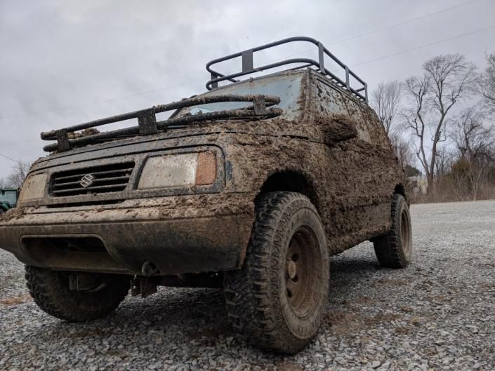 Mud-covered off-road SUV parked on a gravel path under a cloudy sky.