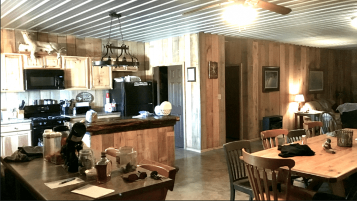 Rustic open kitchen and dining room with wooden table, bar stools, and a dog on a chair