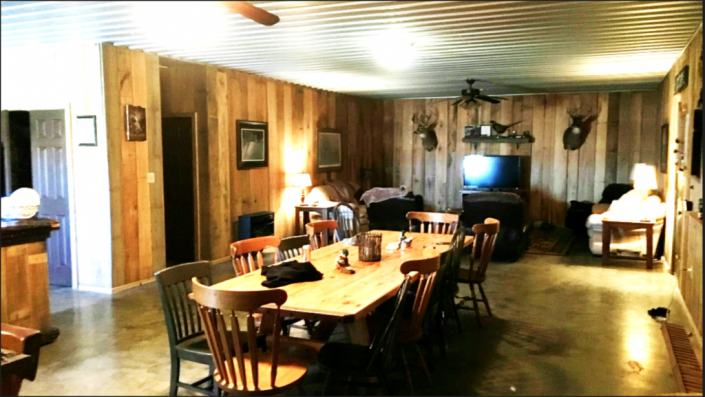 Rustic dining room with long wooden table, chairs, wood-paneled walls, and warm ceiling lights