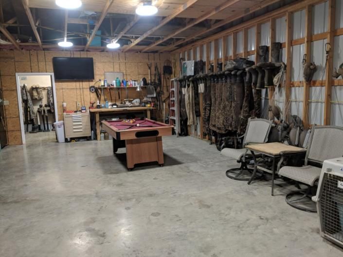 Large garage with concrete floor, workbench, camo gear, folding chairs, and a pool table under exposed rafters