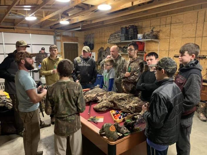 People gathered around a table in a rustic room, examining gear and supplies on display.