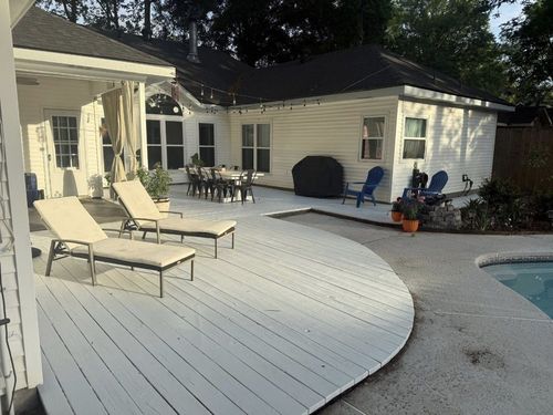 Poolside patio with white deck, lounge chairs, dining table, and a swimming pool beside a house
