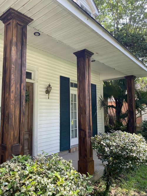 Front porch of a white house with weathered wooden columns and shrubs in front