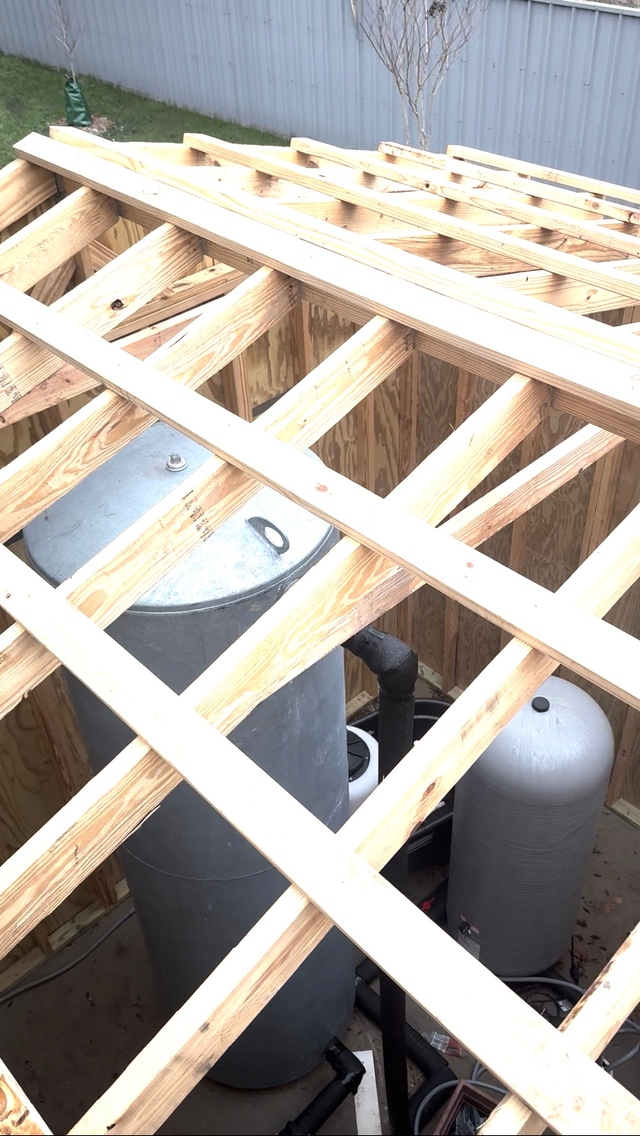 Wooden roof framing over outdoor HVAC units beside a corrugated metal wall.