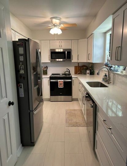 Narrow modern kitchen with white cabinets, stainless steel appliances, and bright countertops