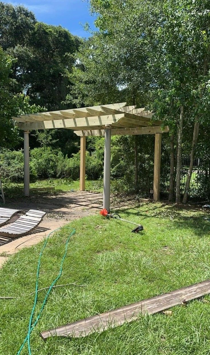 Wooden pergola in a grassy backyard with trees and stepping stones nearby