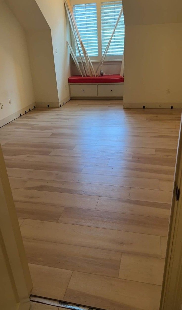 Empty room with light wood floor, white walls, and a window with blinds at the far end.