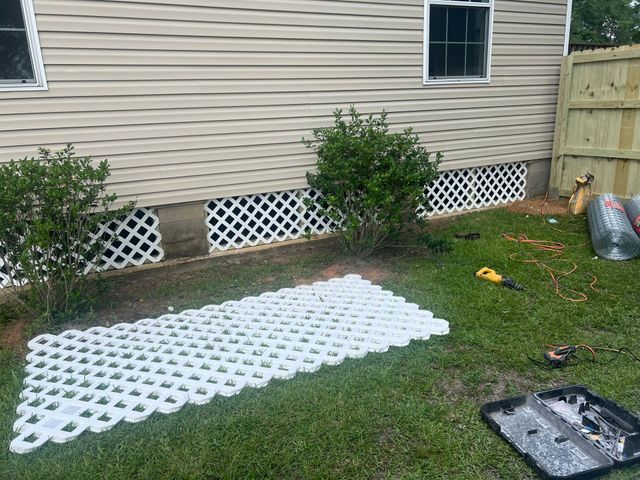 White lattice panels laid on grass beside a house, with shrubs and a fence in the yard.