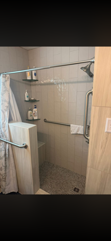 Small bathroom shower with beige tile, glass door, shelves, and a towel hanging on the side.