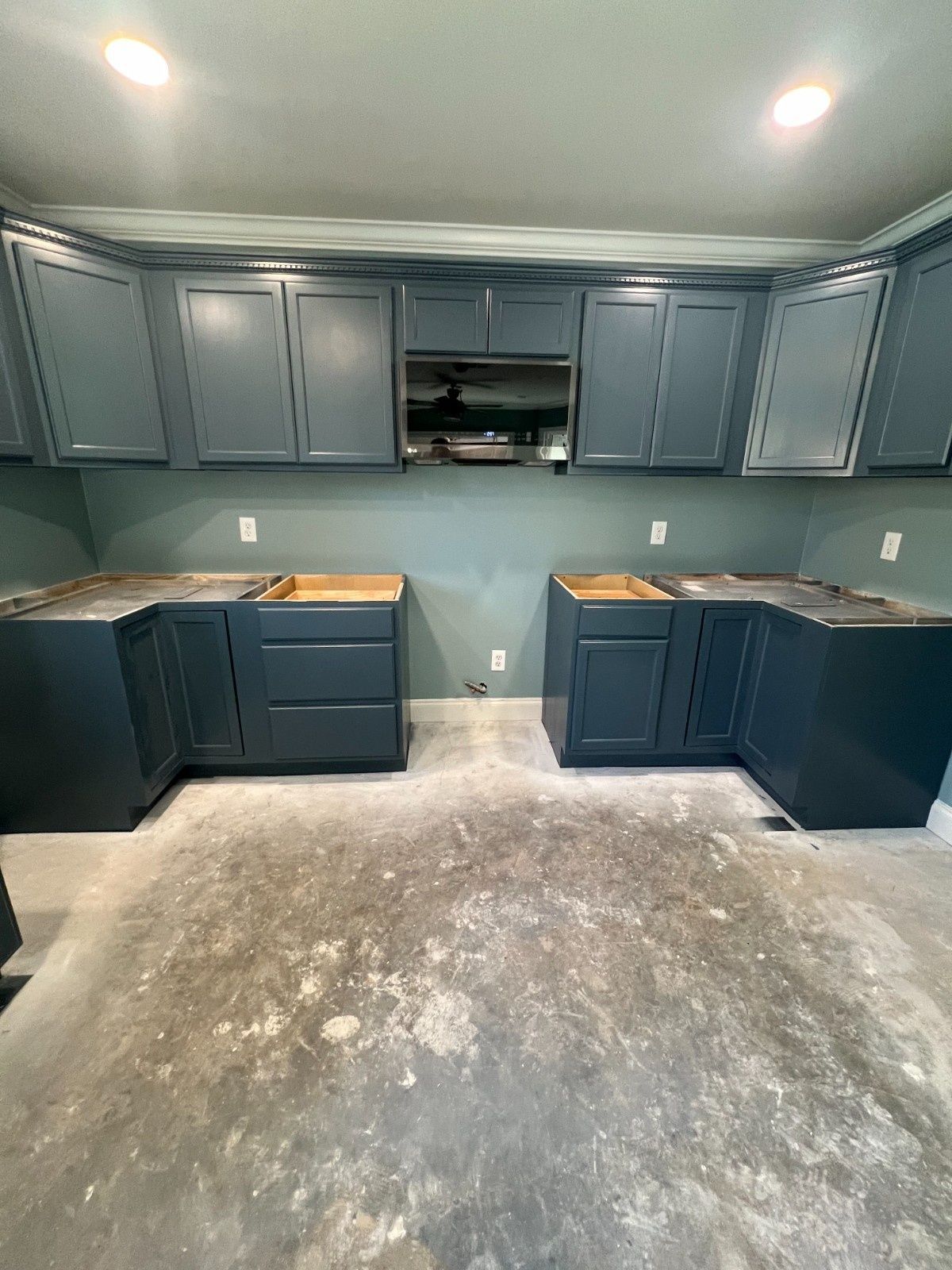 Unfinished kitchen with dark blue cabinets, teal walls, and exposed concrete floor.