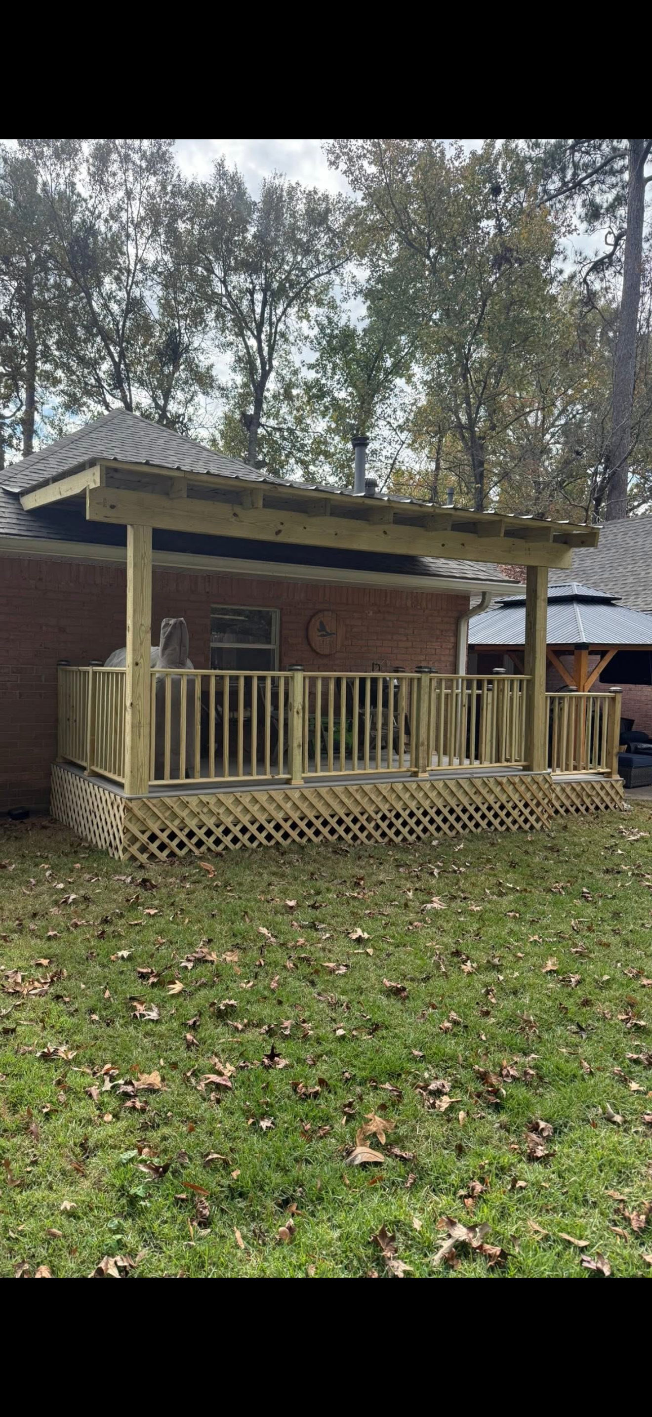 Small brick house with a wooden porch and railings, surrounded by trees and a grassy yard.
