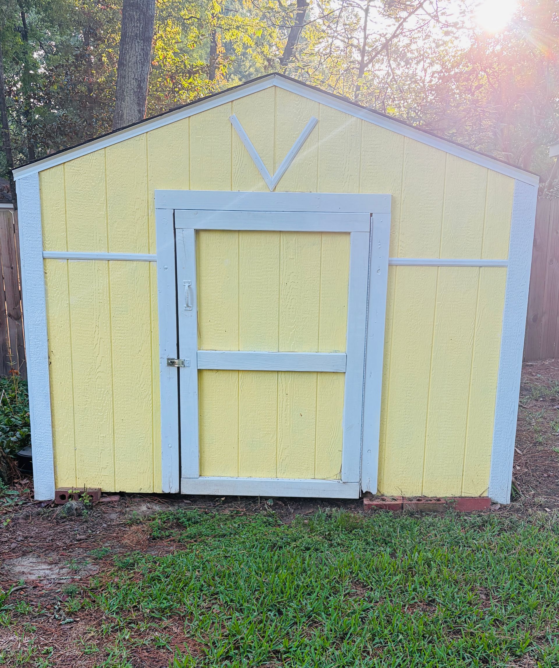 Small tan shed with a pale purple door and trim, set outdoors at dusk