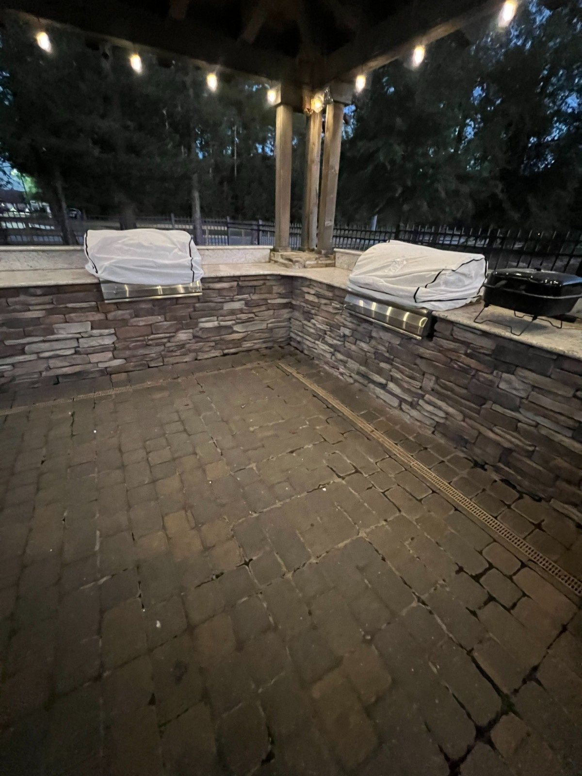 Brick patio with built-in benches under a wooden pergola, covered by white tarps at dusk.