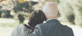 Two people seen from behind, standing close together outdoors in a sunlit park