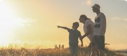 Three people standing in a field at sunset, one pointing toward the horizon.