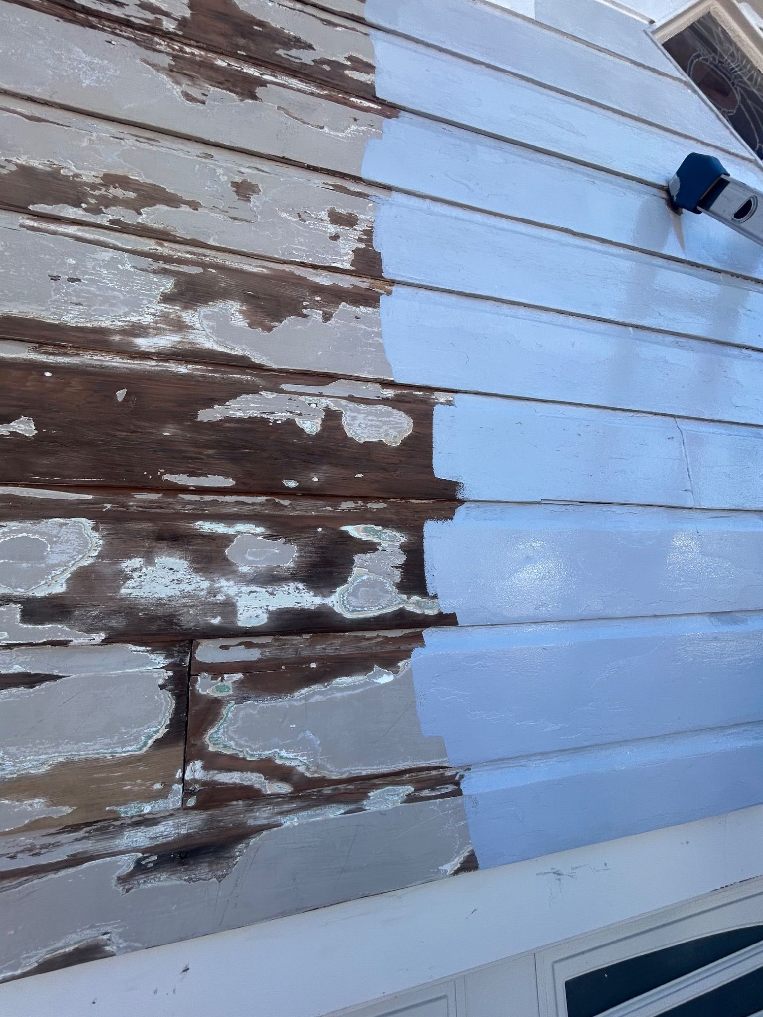 Peeling brown paint on weathered wooden siding beside a blue exterior wall