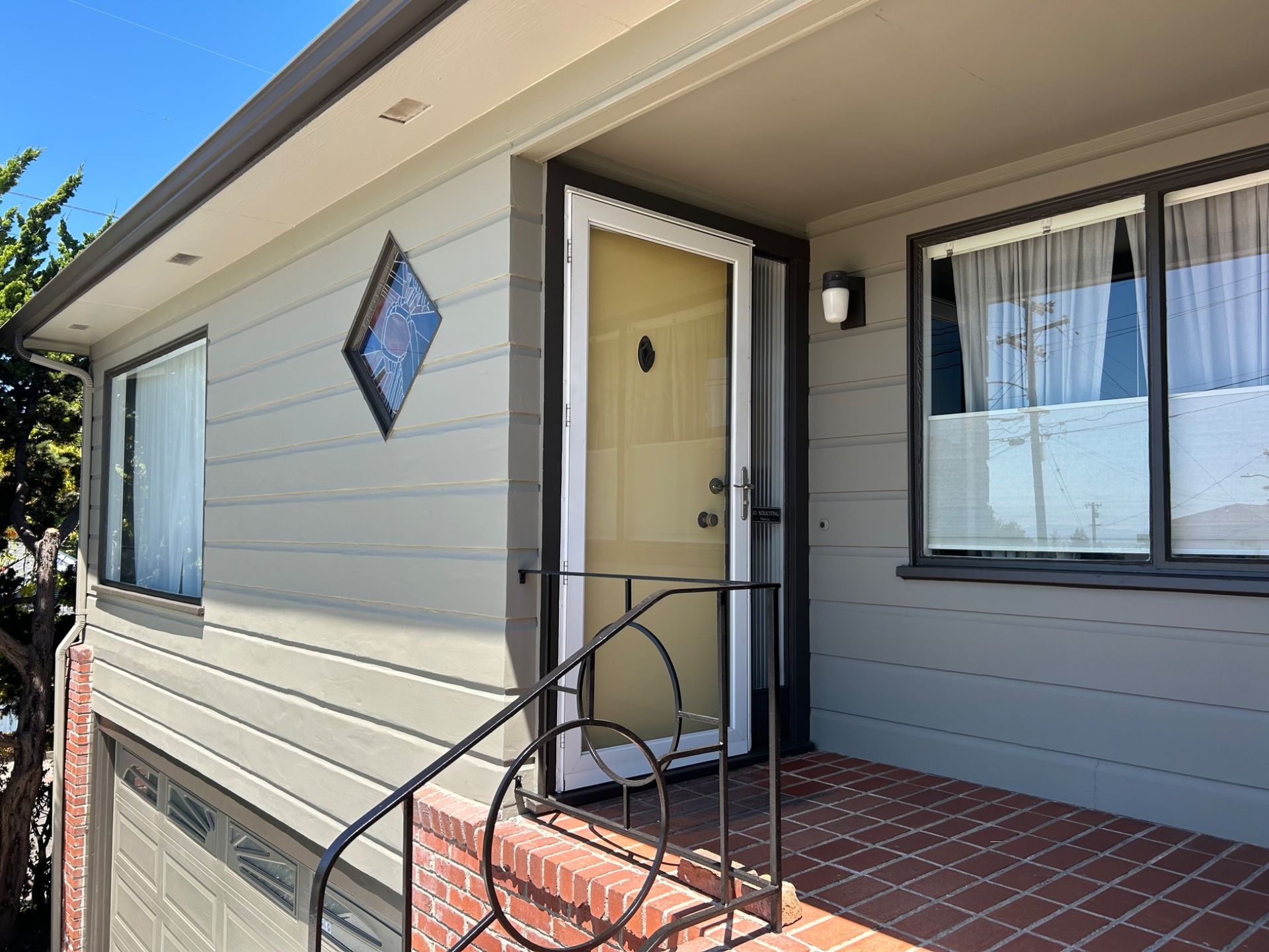Front porch of a beige house with a yellow door, brick steps, and black railing.