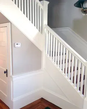 Interior staircase with white railings, beige walls, and wooden floor trim