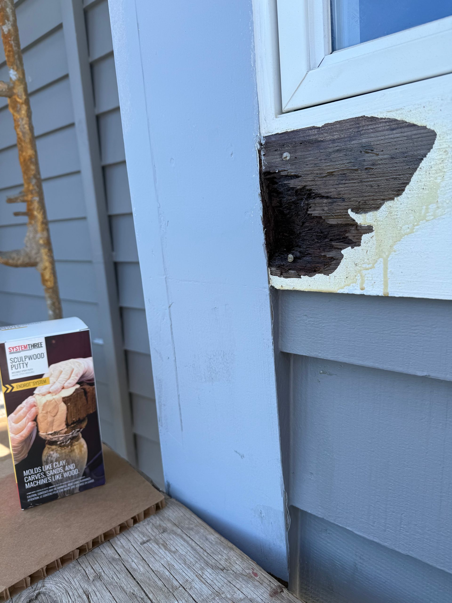 Exterior house wall with peeled white paint, blue siding, and a cardboard box on the ground