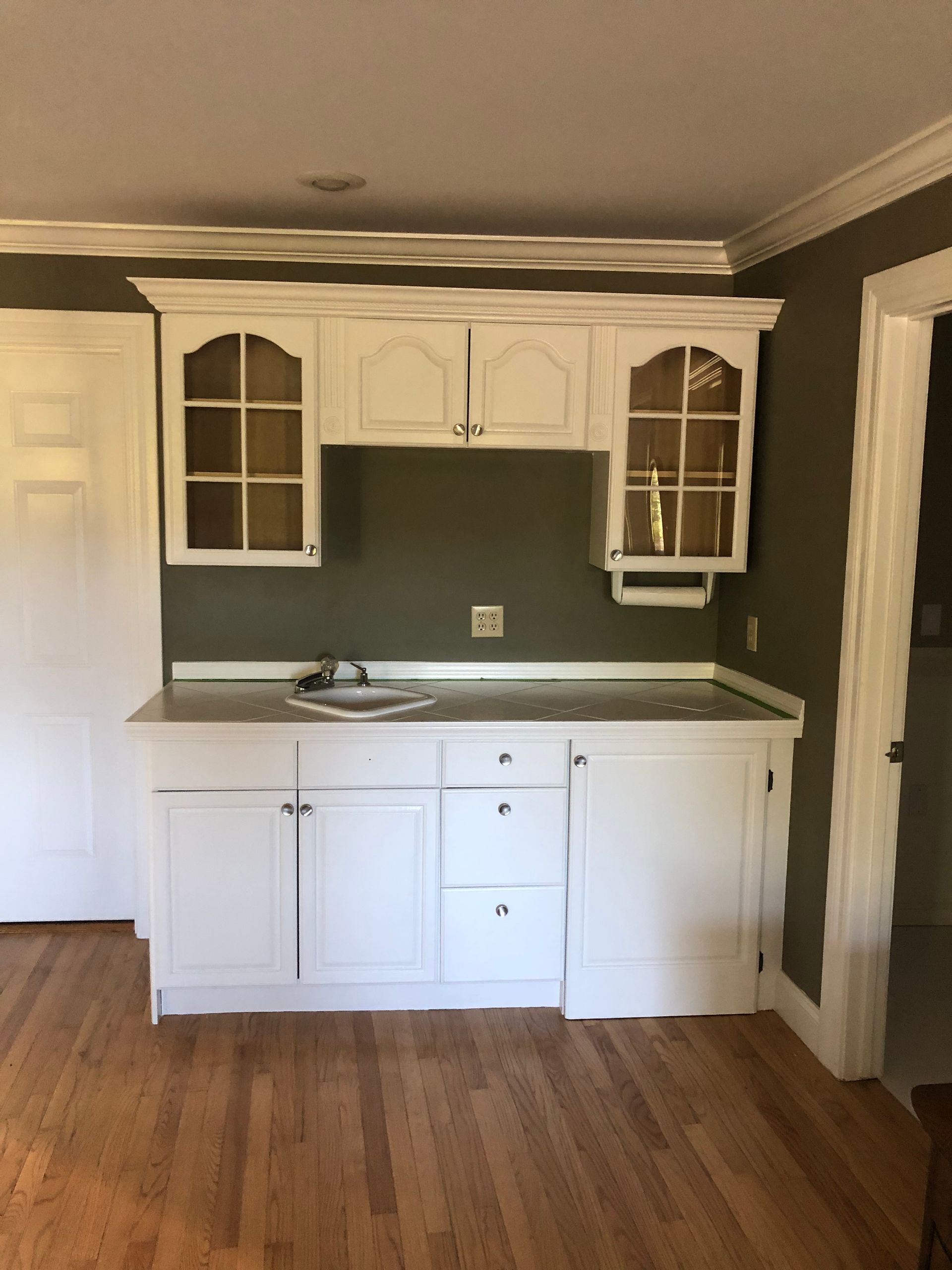 Small white kitchen with cabinets, sink, stove, and hardwood floors against a dark wall.