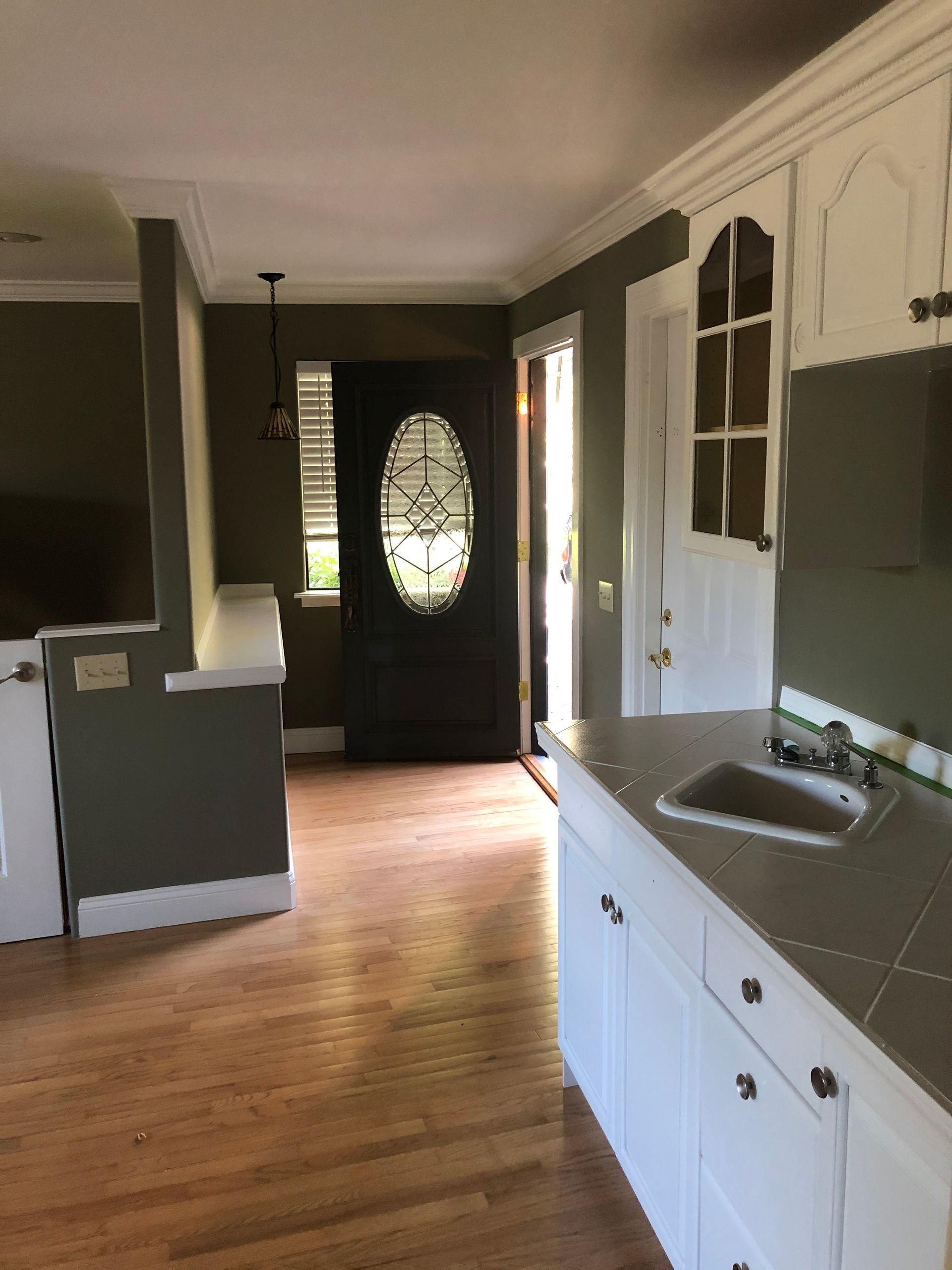 Bright kitchen with white cabinets, gray countertops, wood floor, and a black front door with oval glass.