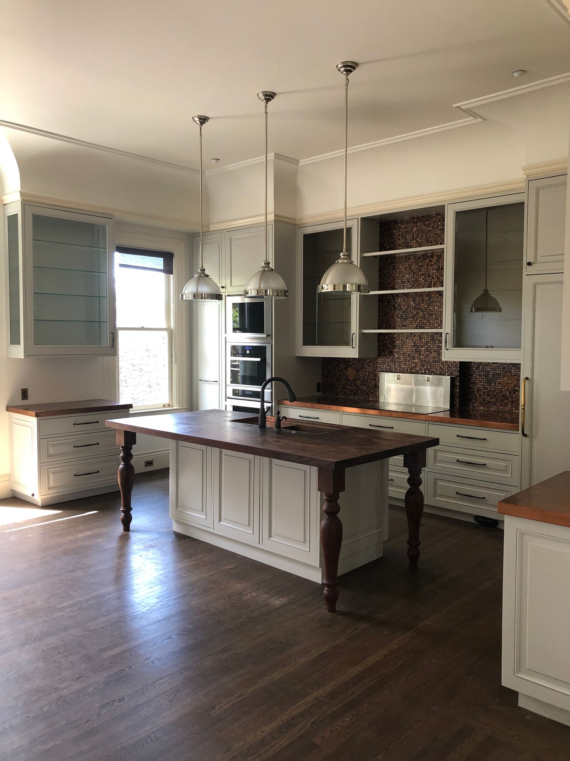 Bright kitchen interior with dark wood island, white cabinets, pendant lights, and large windows