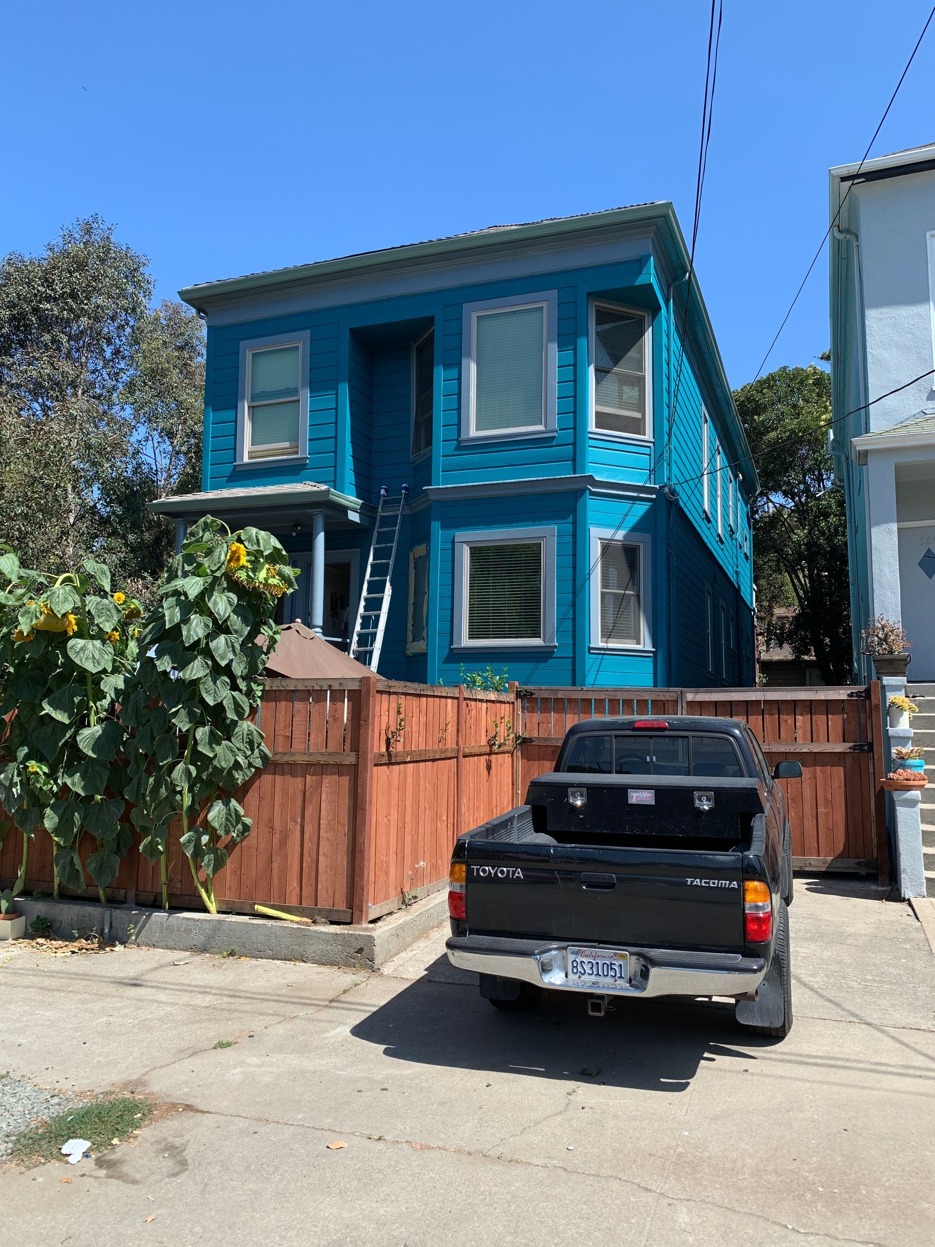 Bright blue two-story house with a black pickup truck parked in front and a wooden fence.