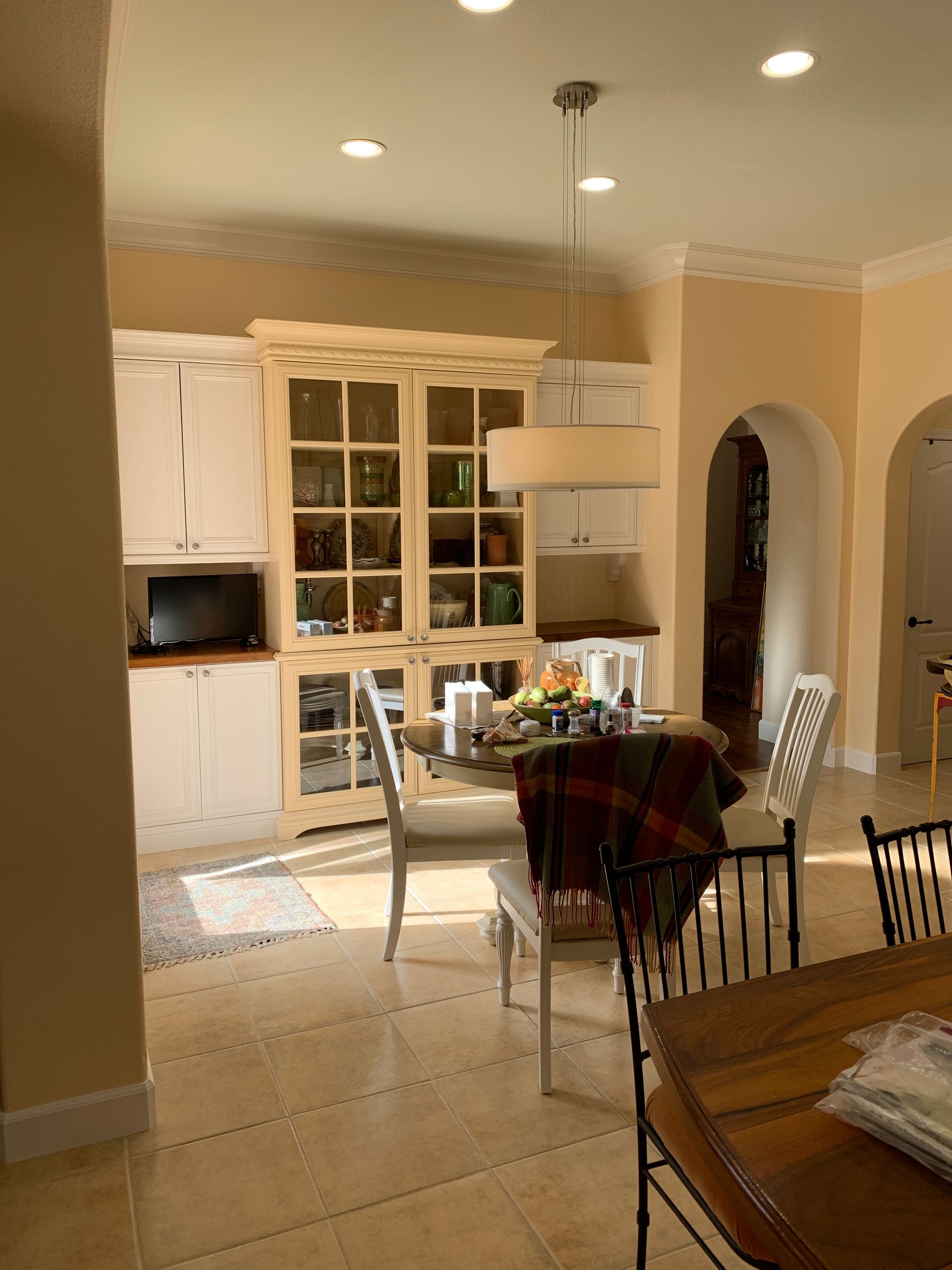 Bright kitchen with white cabinets, beige walls, and a dining table under hanging lights