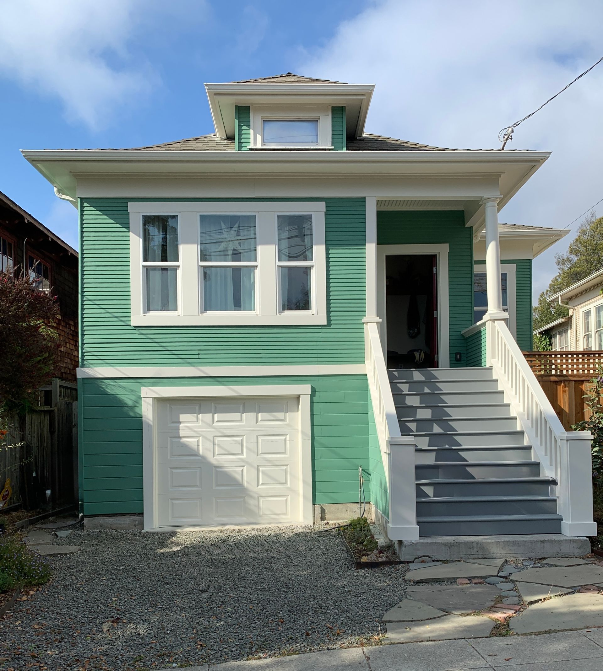Green house with white trim, garage, and front staircase under a blue sky