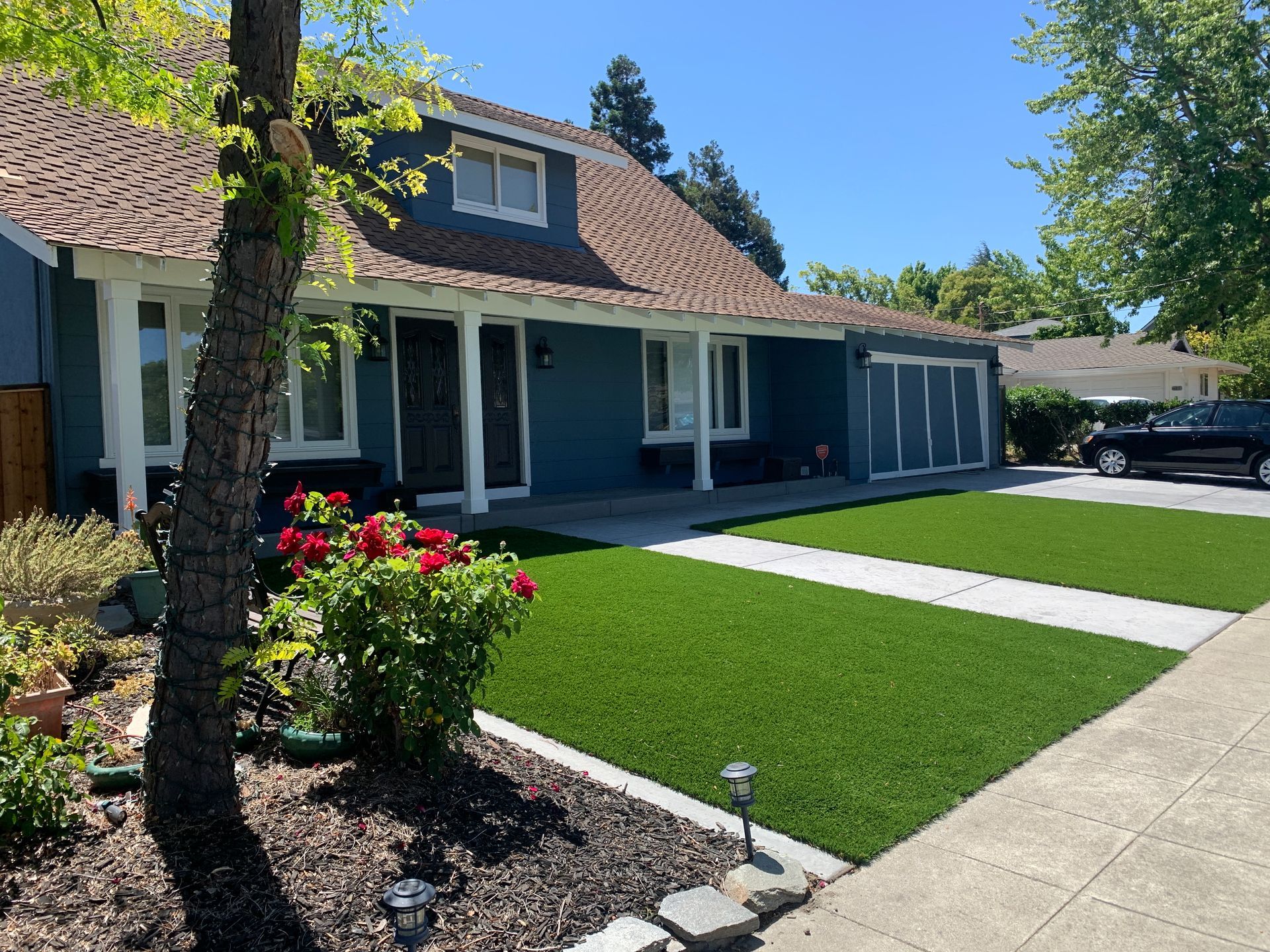 Blue house with manicured lawn, red flowers, and a driveway under a bright sky