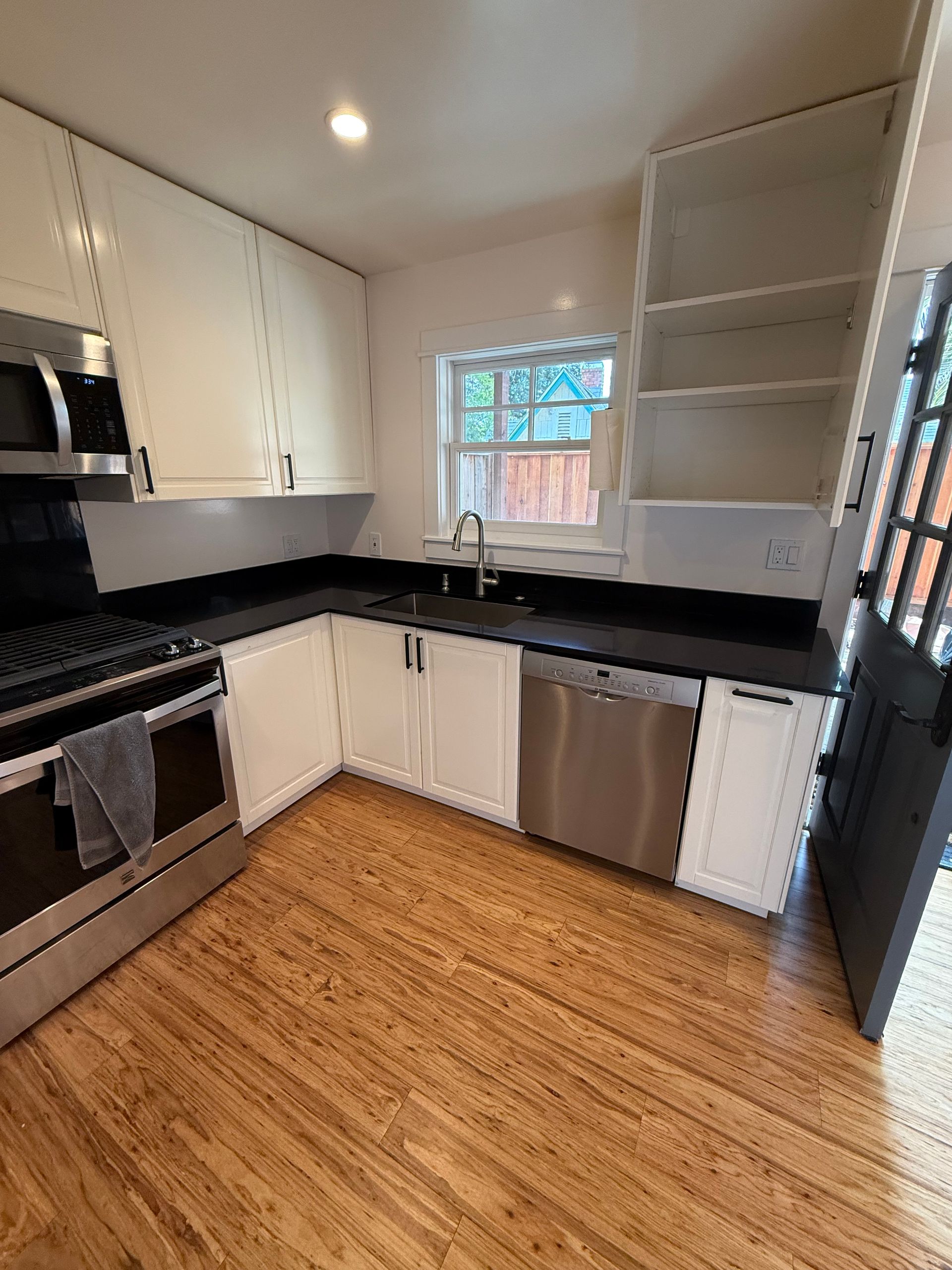 Small modern kitchen with white cabinets, black countertops, stainless appliances, and hardwood floor