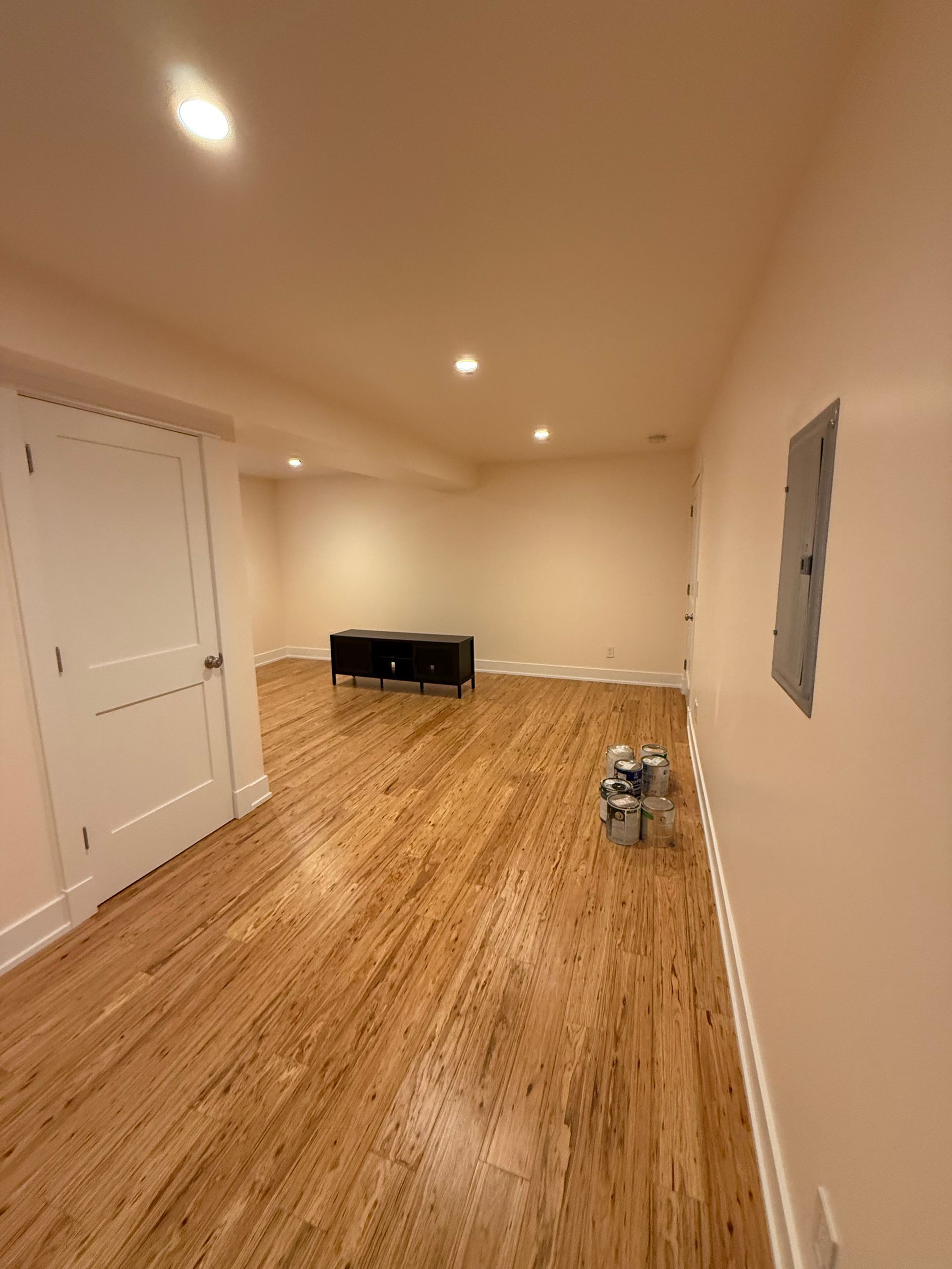 Empty beige room with hardwood floors, recessed lights, a small desk, and a chair near the back wall.