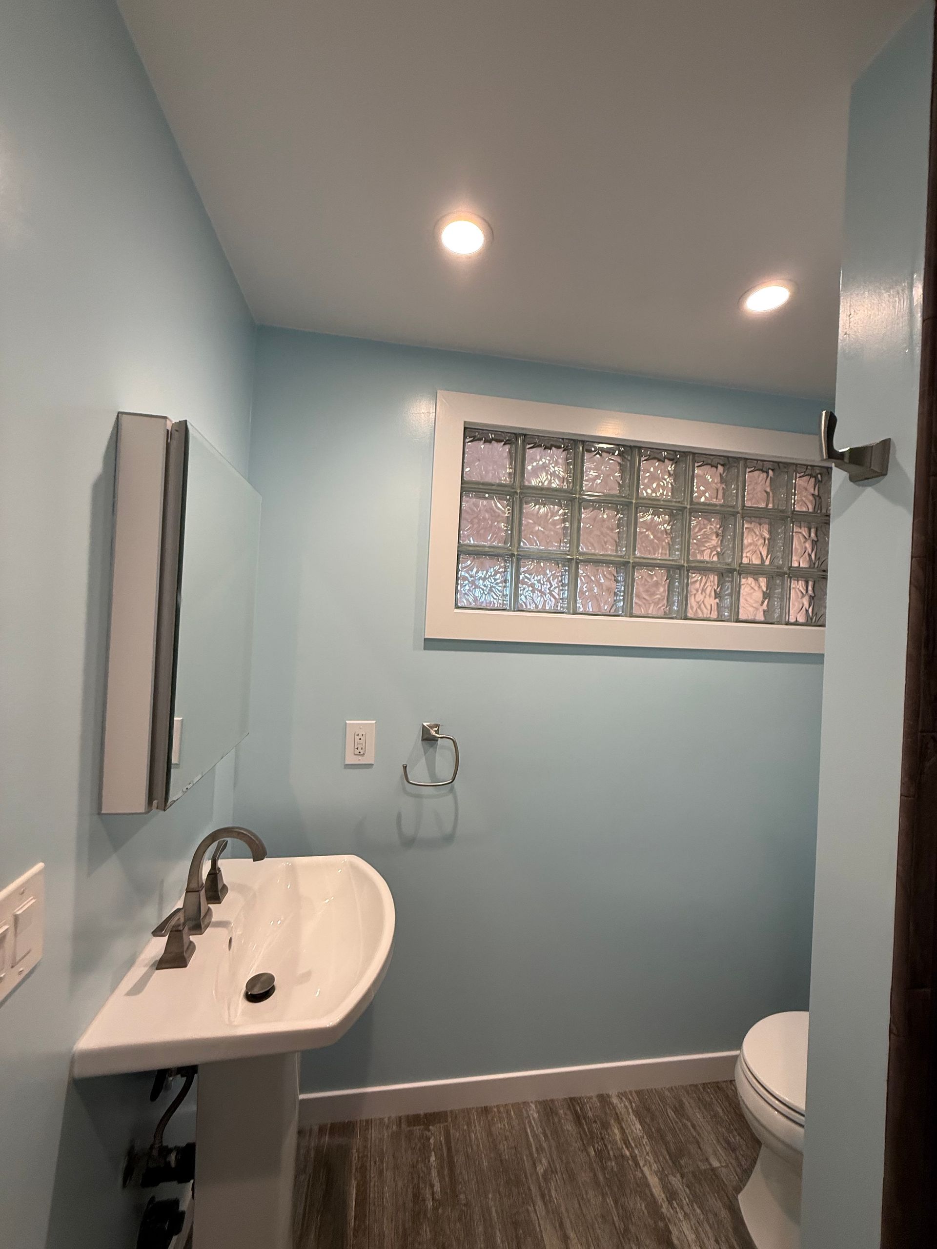 Small light-blue bathroom with pedestal sink, toilet, window, and tiled floor