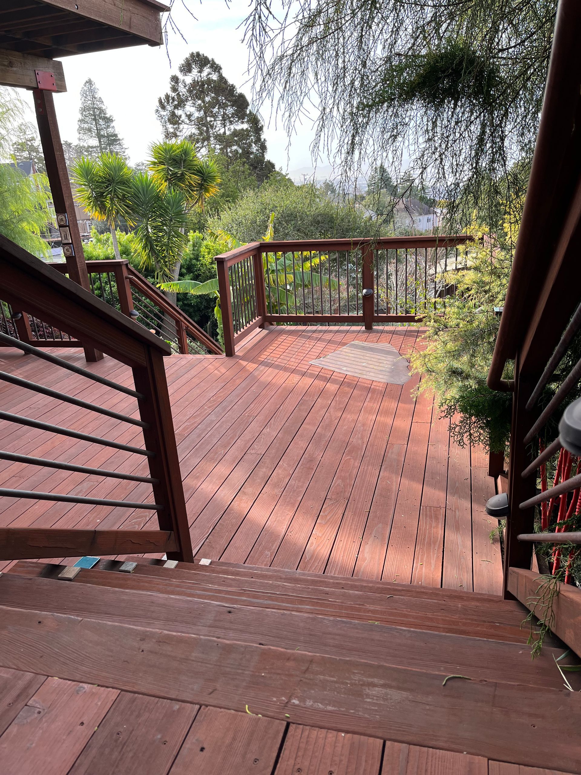 Wooden deck stairs leading to a sunlit outdoor patio with greenery beyond
