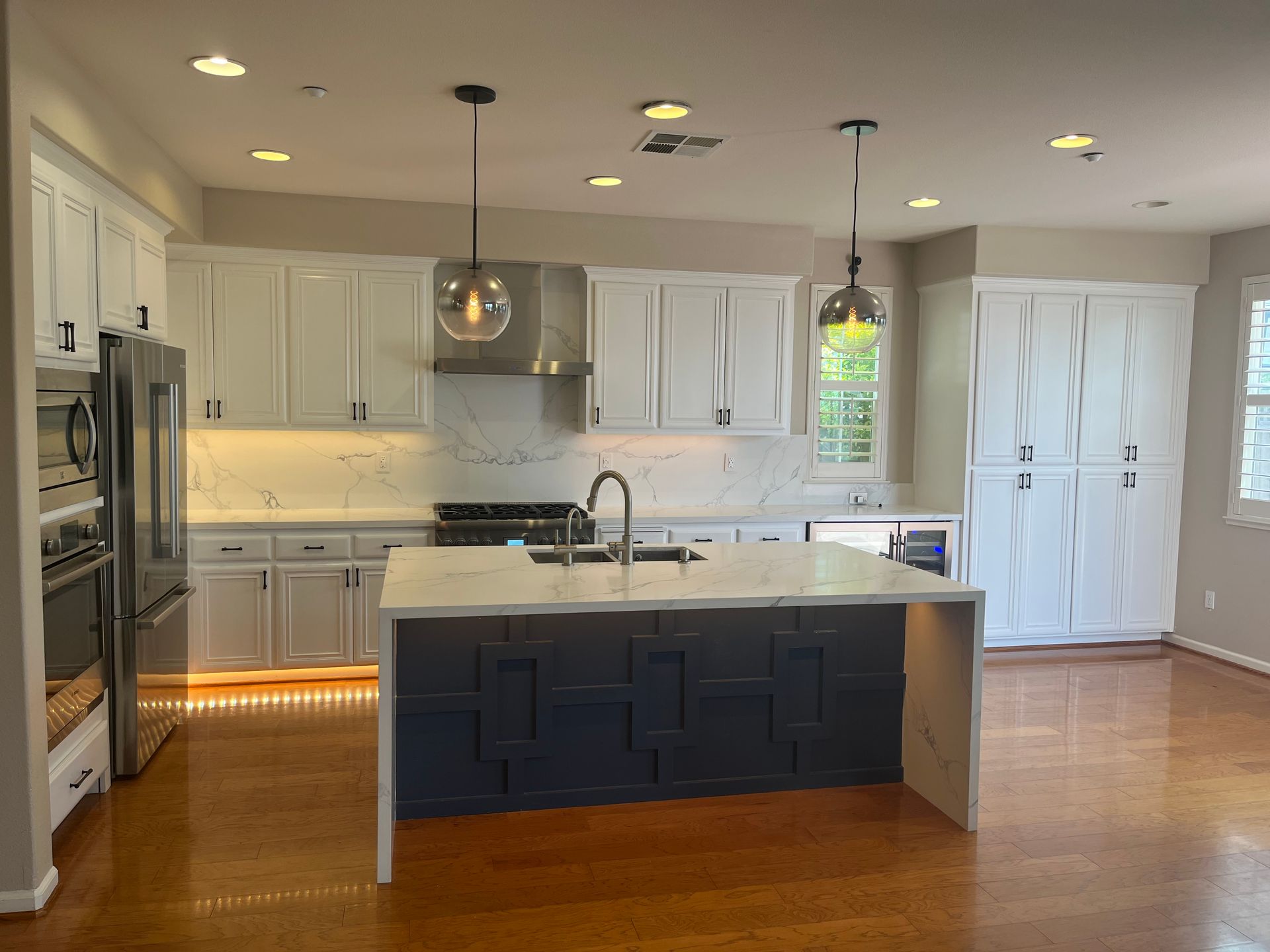 Bright modern kitchen with white cabinets, island, stainless appliances, and hardwood floors