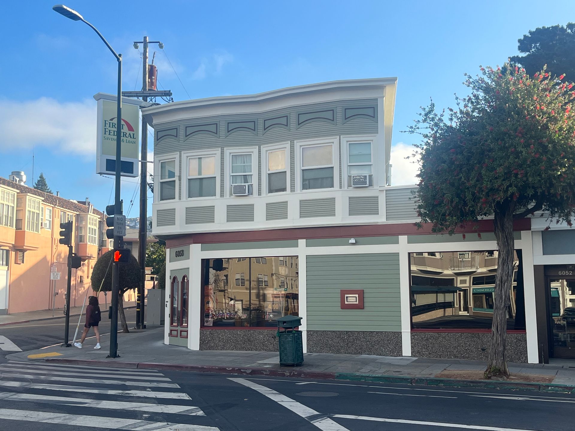 Street corner with a white two-story storefront under a blue sky, beside a crosswalk and traffic light.