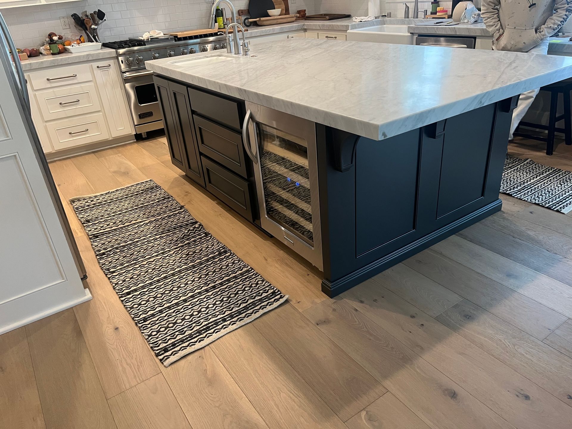 Kitchen island with white countertop, dark cabinets, and built-in storage on a light wood floor.