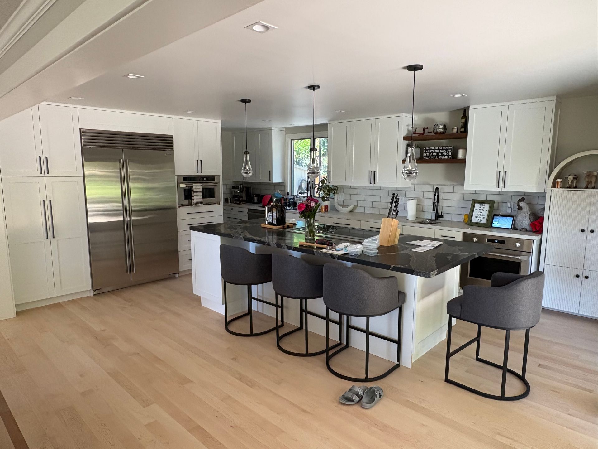 Modern white kitchen with stainless steel fridge, island seating, and open shelving