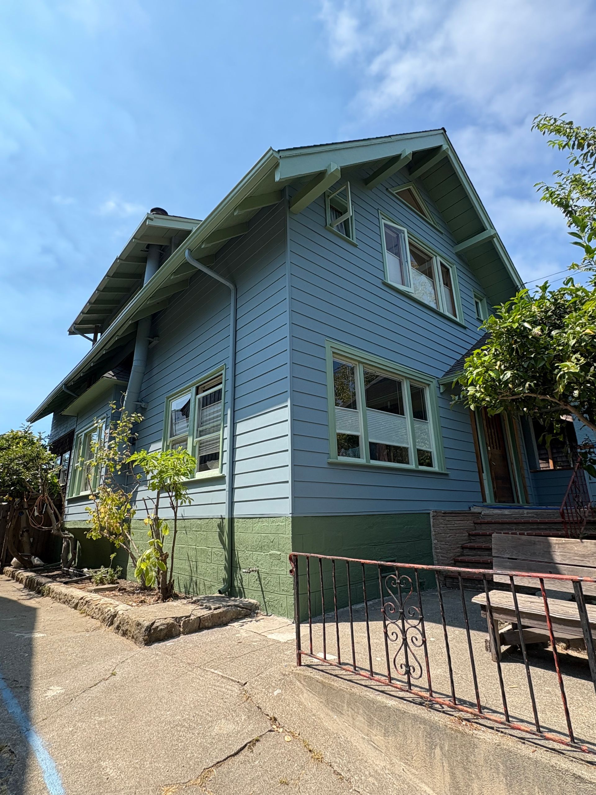 Blue house with white trim and a small front yard behind a black fence under a sunny sky