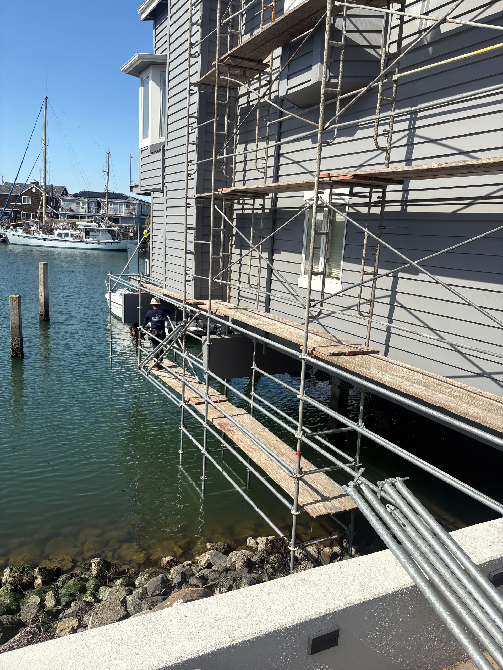 Scaffolding on a waterfront building beside a marina, with water and docks in the background
