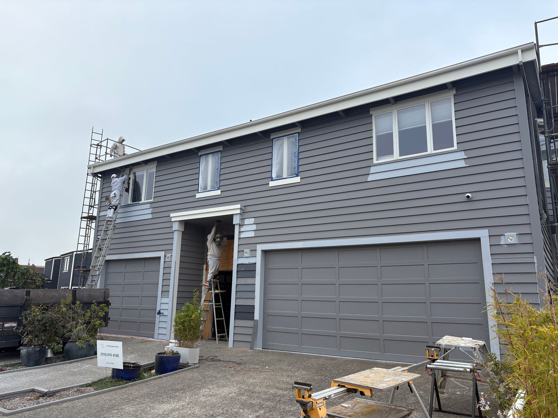 Gray two-story house with new siding, garage doors, and construction materials in the driveway
