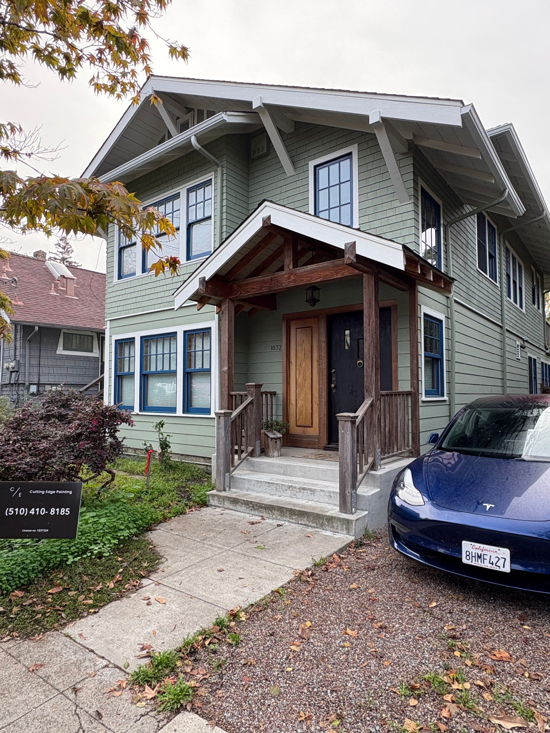 Two-story green house with front porch and blue car parked in driveway