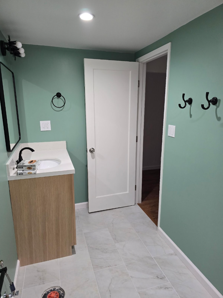 Small bathroom with mint green walls, white door, sink vanity, and black wall hooks.