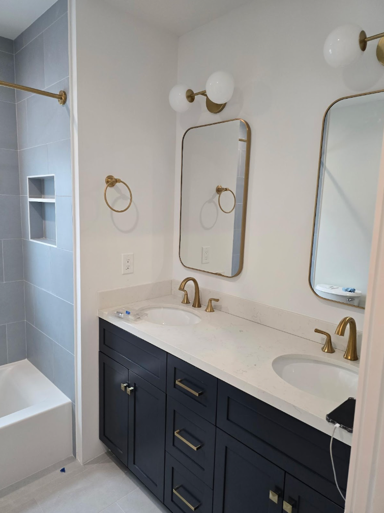 Bright bathroom vanity with navy cabinets, white countertop, gold fixtures, and mirrored sconces.