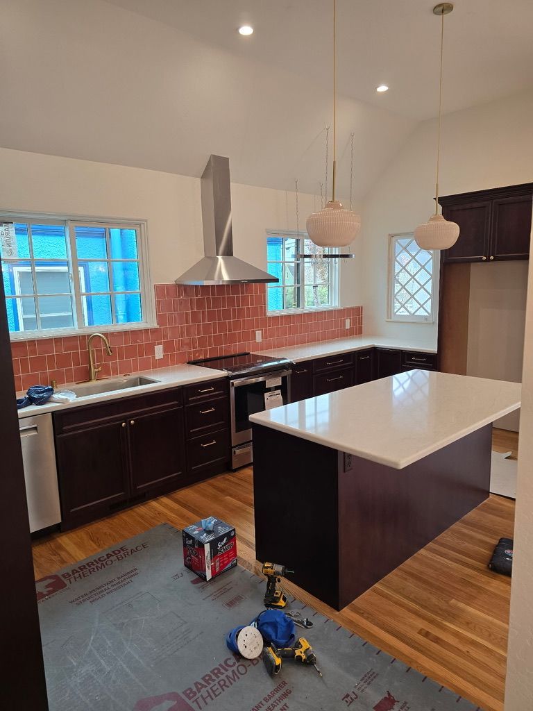 Modern kitchen with dark cabinets, white island, red tile backsplash, and cleaning supplies on the floor