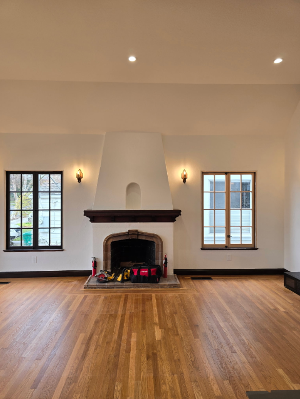 Empty living room with hardwood floors, white fireplace, and two windows on either side
