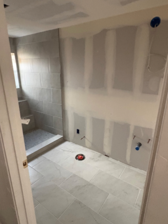 Partially renovated bathroom with tiled shower, white floor, and unfinished drywall walls