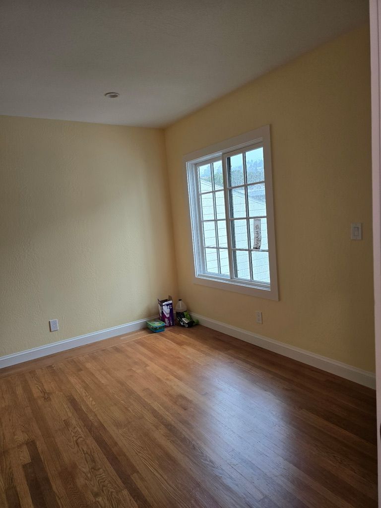 Empty beige room with hardwood floors and a window on the right side