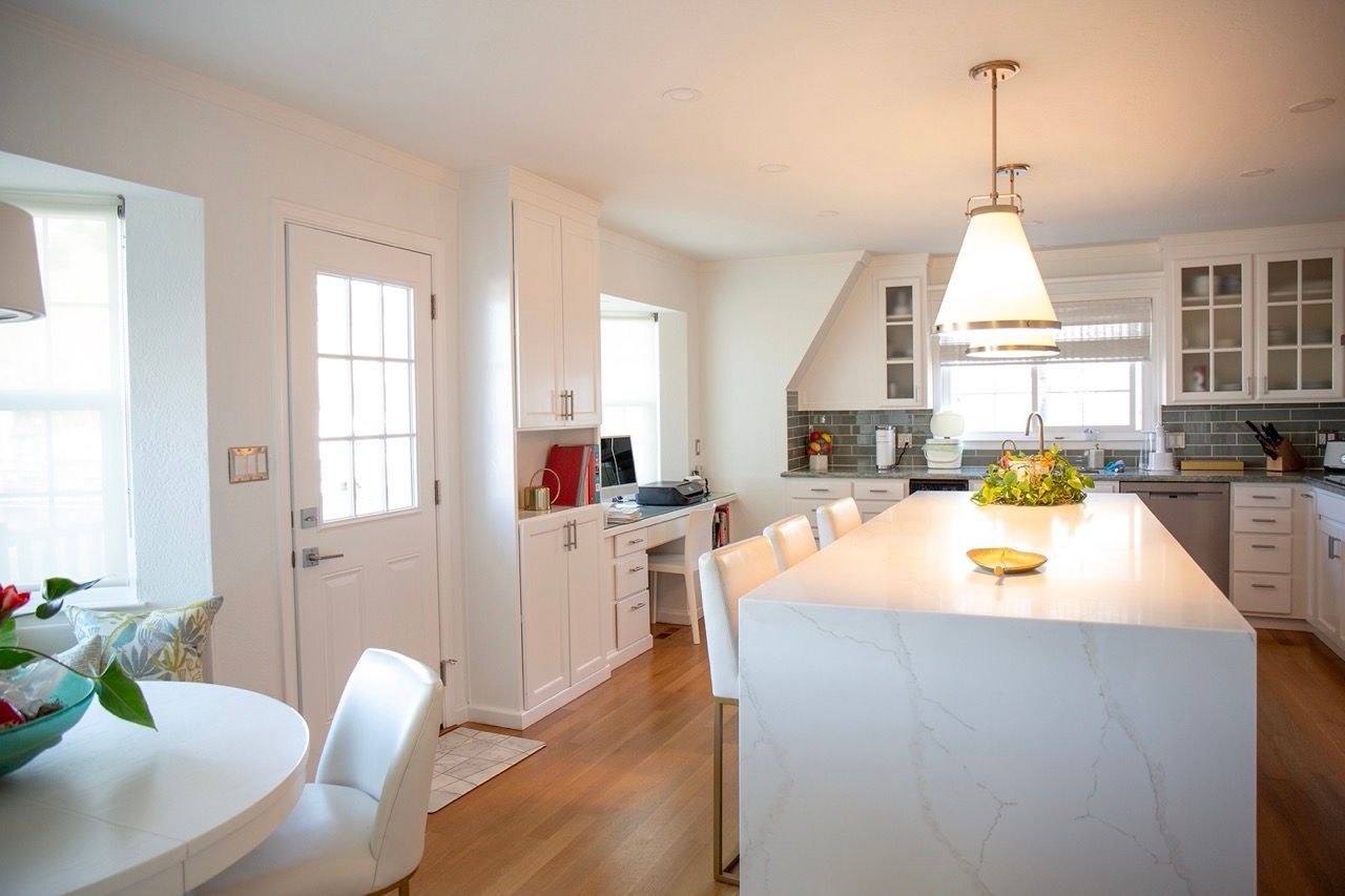 Bright white kitchen with island, pendant light, and dining nook by a window